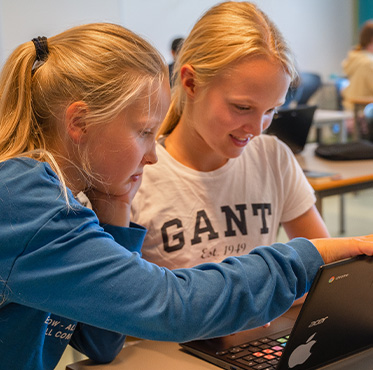 To jenter som spiller på en Chromebook. Den ene jenta smiler, mens den andre jenta peker på skjermen